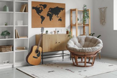 Rahat koltuk, çekmeceler, gitar ve dünya haritası oturma odasının iç tarafındaki beyaz duvarda.