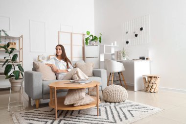 Aydınlık oturma odasındaki gri koltukta oturan genç kadın.