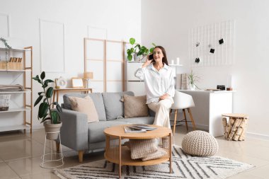 Aydınlık oturma odasındaki gri koltukta cep telefonuyla konuşan genç bir kadın.