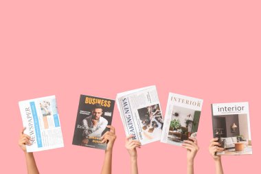 Farklı dergilere ve pembe arka planda gazetelere sahip kadın elleri.