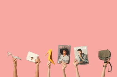 Farklı dergilere sahip kadın elleri, şık çantalar ve pembe arka planda topuklu ayakkabılar.