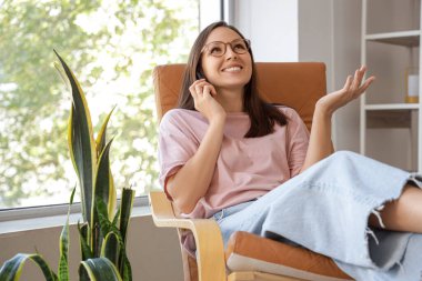 Evdeki koltukta cep telefonuyla konuşan genç bir kadın.