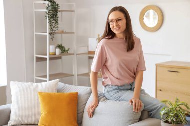 Gözlüklü genç kadın evdeki yumuşak kanepede oturuyor.