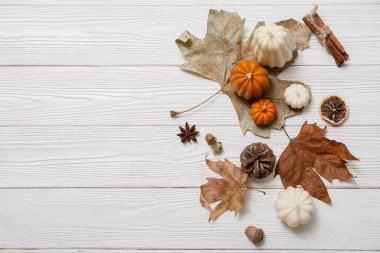 Balkabağı şeklinde mumlar, düşmüş yapraklar ve hafif ahşap arka planda baharatlarla sonbahar kompozisyonu