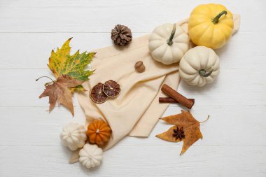 Mumlu sonbahar kompozisyonu, taze balkabakları ve açık ahşap arka planda düşmüş yapraklar.