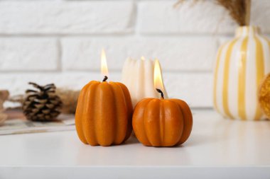 Evdeki beyaz tuğla duvarın yanındaki raf ünitesinde balkabağı şeklinde mumlar yakıyor.