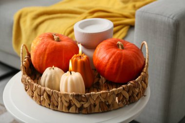 Evdeki taburede balkabağı şeklinde yanan mumlarla dolu hasır sepet, yakın plan.