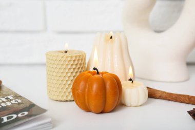 Evdeki beyaz tuğla duvarın yanındaki raf ünitesinde balkabağı şeklinde mumlar yakıyor.