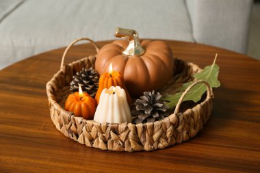 Wicker basket with burning candles in shape of pumpkins and forest bumps on coffee table at home, closeup