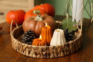 Evdeki sepetin üzerinde balkabağı şeklinde yanan mumlar ve sehpanın üzerindeki orman çıkıntıları, yakın plan.