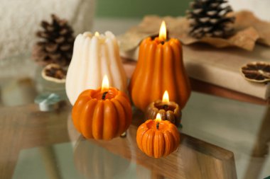 Evdeki kahve masasında balkabağı, kitap ve orman çıkıntıları şeklinde mum yakmak, yakın plan.