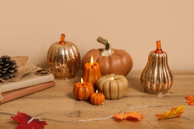 Sonbahar yapraklı balkabağı şeklinde mumlar yakmak ve evdeki bej duvarın yanındaki raflarda kitaplar.