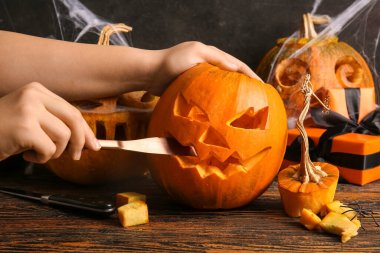 Kahverengi ahşap arka planda Cadılar Bayramı için balkabağı oyan hediye kutuları ve bıçak taşıyan bir kadın.