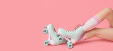 Pembe arka planda paten giyen eski moda paten giyen genç bir kadının bacakları.