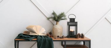 Noel feneri, yanan mum, vazo ve kitap gri duvarın yanındaki masada.