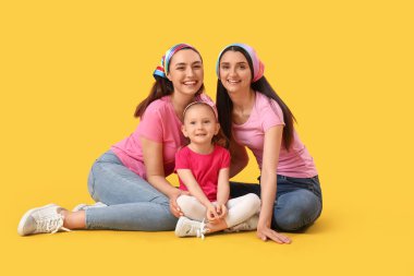 Sarı arka planda oturan evlat edinilmiş küçük kızı olan genç lezbiyen çift.