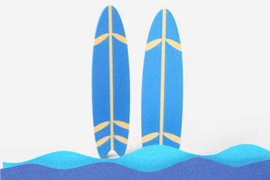 Mavi zemin üzerinde kağıt dalgaları ve mini sörf tahtaları olan yaratıcı kompozisyon