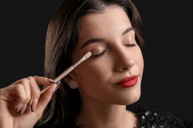 Siyah arka plana göz farı süren fırçalı güzel bir genç kadın.