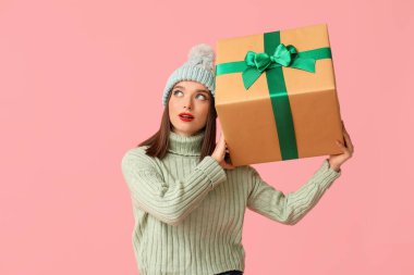 Genç bir kadın pembe arka planda Noel hediyesi kutusunu tutuyor.