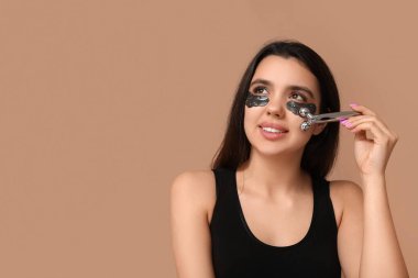 Göz altı bantları olan güzel genç bir kadın masaj aletini renk arka planında kullanıyor.