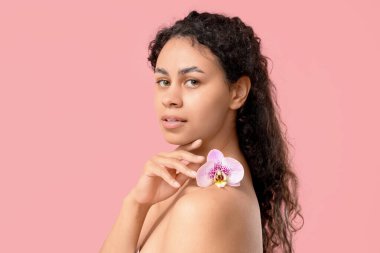 Pembe arka planda orkide çiçeğiyle güzel bir Afro-Amerikalı kadın.