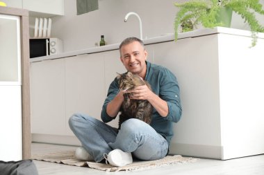 Evde tatlı kedisi olan olgun bir adam yerde oturuyor.