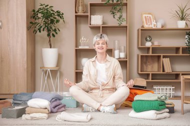 Evde meditasyon yapan bir yığın temiz elbisesi olan güzel genç bir kadın.