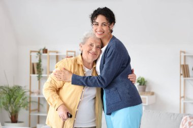 Genç Afro-Amerikalı kadın sağlık görevlisi huzurevinde yaşlı kadına sarılıyor.