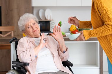 Huzurevindeki genç Afro-Amerikalı kadın sağlık çalışanının yemeğini reddeden yaşlı bir kadın.