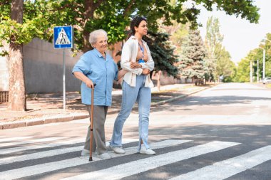 Genç Afro-Amerikalı kadın sağlık görevlisi dışarıda yaşlı bir kadının geçişine yardım ediyor.