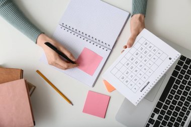 Takvim ve dizüstü bilgisayarı olan genç bir kadın ofiste planlar yapıyor.