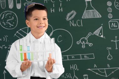 Kimya dersinde kimya tahtasının yanında kimya mataraları olan şirin bir çocuk.