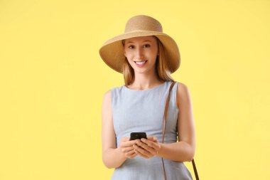 Şapkalı güzel bir kadın sarı arka planda cep telefonuyla sohbet ediyor.