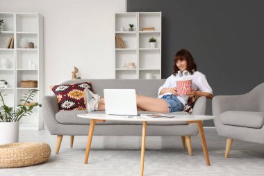 Patlamış mısırlı güzel bir kadın evde dizüstü bilgisayardan film izliyor.