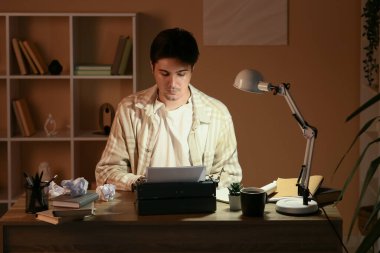 Klasik daktilosu ve lambası olan genç bir yazar masada çalışıyor.