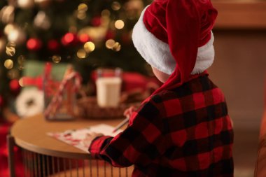 Noel arifesinde evde Noel Baba 'ya mektup yazan sevimli bir çocuk.