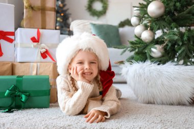 Noel Baba şapkalı şirin küçük kız evde yerde yatıyor.