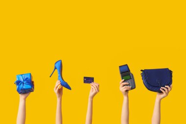 Aksesuarları, ödeme terminali ve sarı arka planda Noel hediye kutusu olan birçok kadın eli.