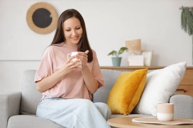 Evdeki kanepede oturan bir fincan kahveyle genç bir kadın.