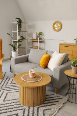 Ayna, gri kanepe ve raf üniteli aydınlık oturma odasının içi.