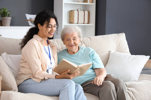 Young African-American female medical worker reading book with elderly woman in nursing home