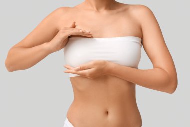 Bandeau bluzlu, gri arka planda güzel göğüsleri olan genç bir kadın. Yakın plan.