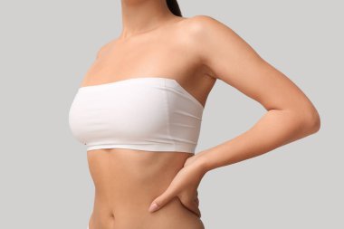 Bandeau bluzlu, gri arka planda güzel göğüsleri olan genç bir kadın. Yakın plan.