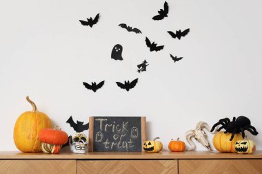 Balkabağı, kafatası, örümcek ve karatahtayla kaplı çekmeceler. TRICK veya kağıt yarasalarla beyaz duvarın yanında tedavi