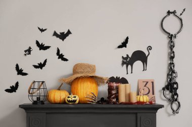 Beyaz duvarın yanındaki şöminede kağıt yarasalar, kedi ve zincirler var.