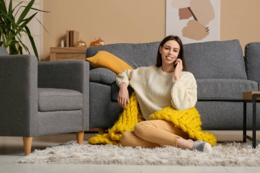 Güzel, sarı ekoseli bir kadın oturma odasında otururken cep telefonu kullanıyor.