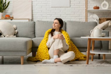 Sıcak sarı ekoseli güzel bir kadın oturma odasında yerde oturuyor.