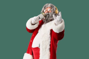 Kulaklıklı Noel Baba yeşil arka planda mikrofonla şarkı söylüyor.