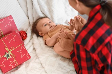 Annesiyle küçük şirin bir bebek ve Noel hediyeleri. Evdeki battaniyeye uzanmış, yakın plan.
