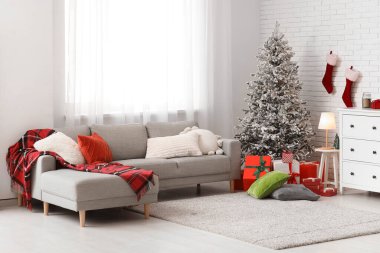 İçinde gri kanepe, Noel ağacı ve hediye kutuları olan şenlikli bir oturma odası.